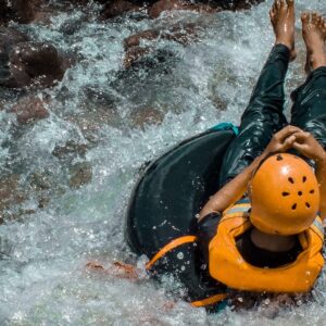 person riding inflatable pool ring on flowing body of water